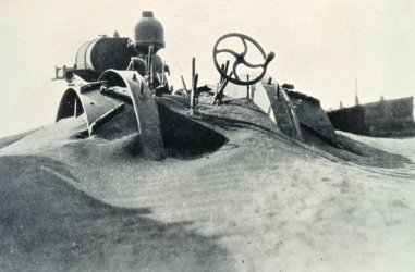 An old black and white photograph of indistinct machinery with levers and a steering wheel covered in sand