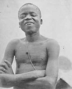 Black and white archive photo of young African man shirtless and smiling with his arms crossed