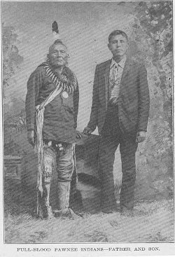 Black and white archive photo from 1912 showing a Native American man in traditional dress next to his son wearing European clothing